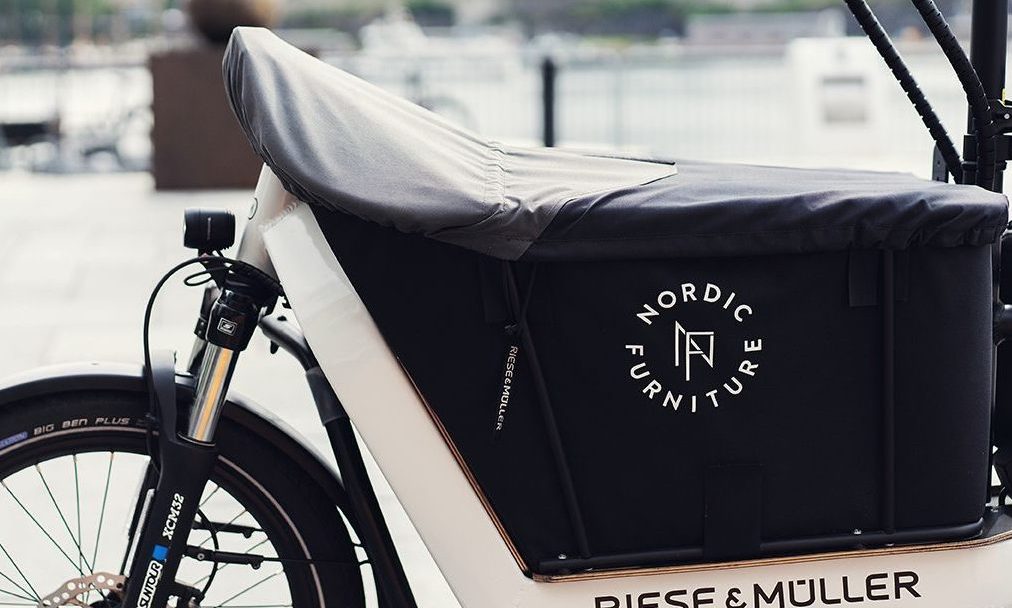 Sett fra siden av en Riese & Müller lastesykkel med et dekket oppbevaringsrom med Nordic Furniture-logoen.