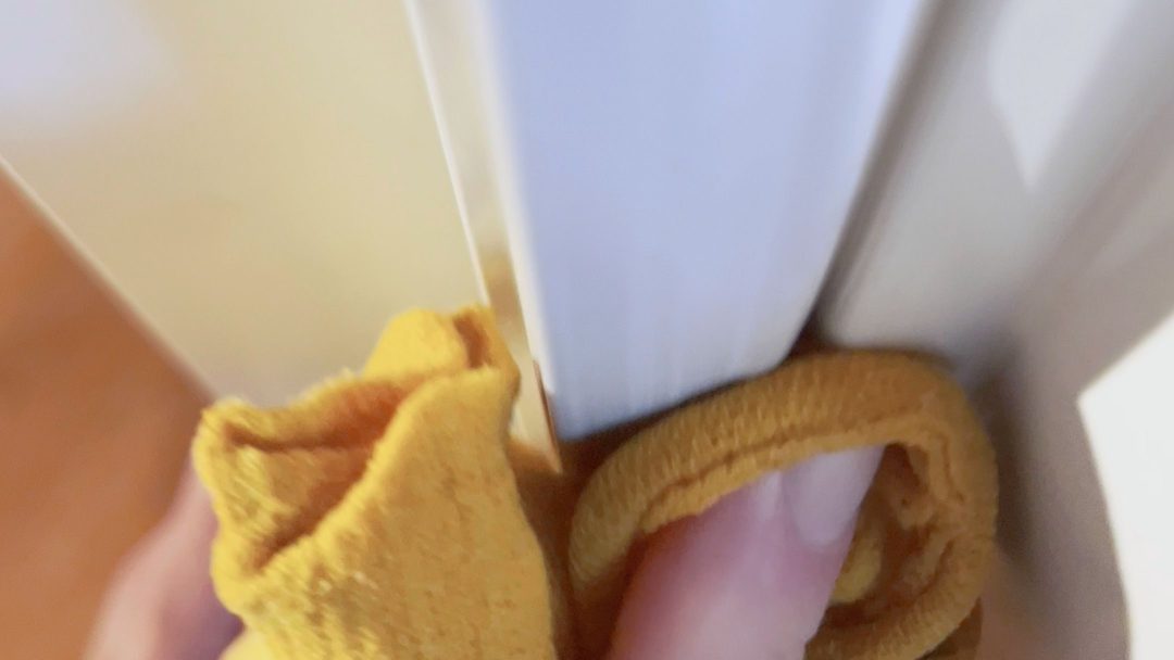En person renser et trangt mellomrom mellom to hvitevarer med en gul klut.