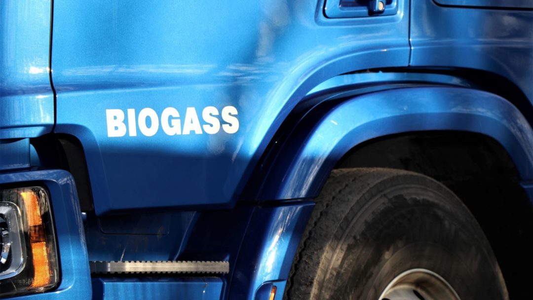 Nærbilde av et blått kjøretøy med ordet Biogass nær forhjulet, som viser dens miljøvennlige innovasjon – et initiativ støttet av Enova-støtten.