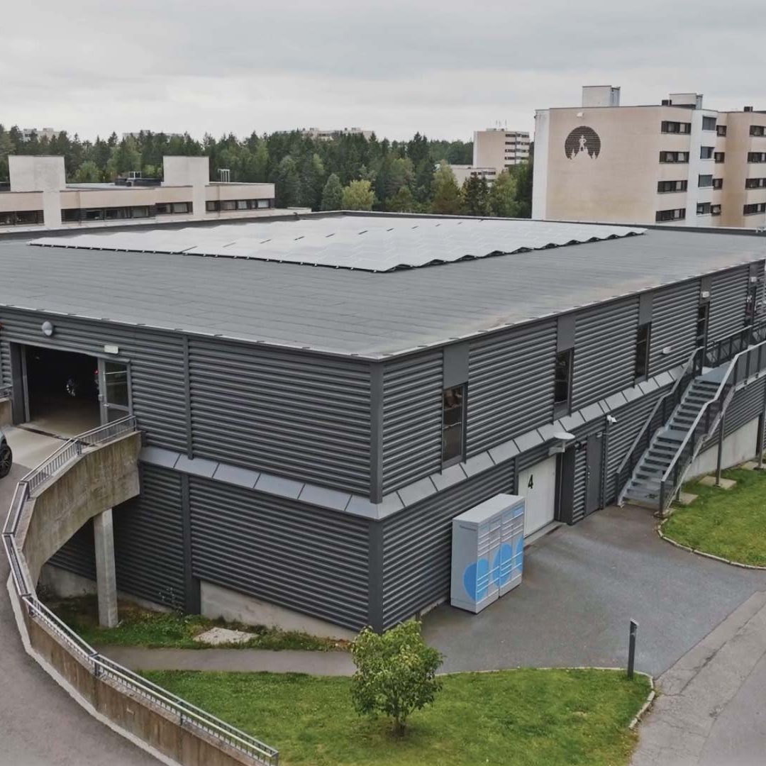 Luftfoto av en grå industribygning, med rampe og utvendig trapp. En hvit bil står parkert på rampen, og understreker KlimaOslos blanding av by- og boligliv, med trær i bakgrunnen blant koselige hjem.