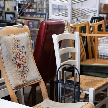 En samling av assorterte brukte møbler fyller oppbevaringsområdet, med tre-, polstrede og metallstoler.