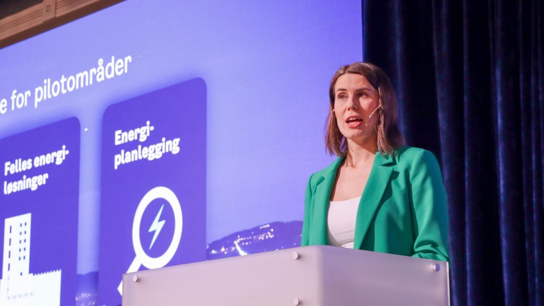 En kvinne som står på et podium og diskuterer energiforsyning foran en skjerm.