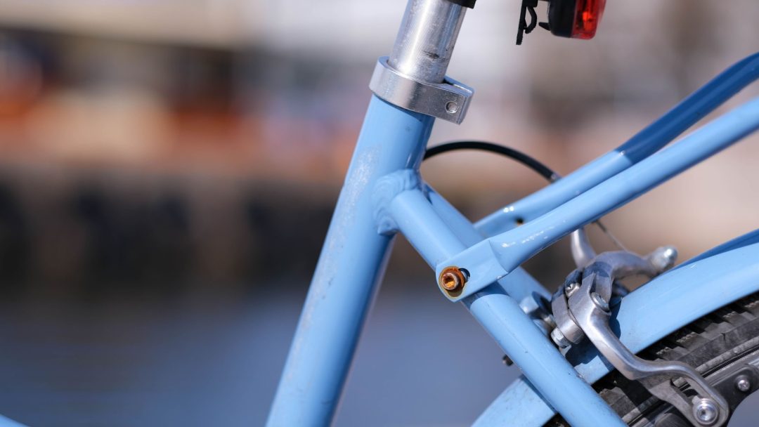 Nærbilde av en lyseblå bruktsykkelramme og bakbrems, med uskarp bakgrunn, som fremhever dens elegante design.