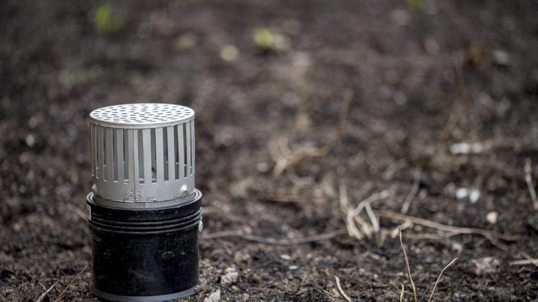 En hvit sylindrisk ventilstruktur dukker opp fra bakken, omgitt av tørr, sparsom vegetasjon – en scene som minner om en klimatilpasningsrapports funn.