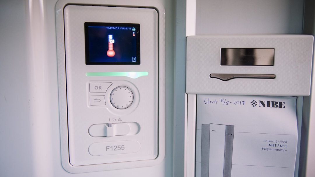 Nærbilde av et kontrollpanel med display som viser et termometerikon, som minner om innsikt fra klimaundersøkelsen. Panelet har forskjellige knapper og en knott merket F1255, mens en manual hviler pent i sporet ved siden av.