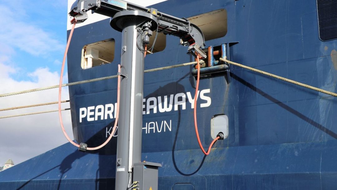 Skipets skrog, merket med Pearl Seaways og København, viser dokkingutstyr og tau festet til pullerter. Mens fartøyet forbereder seg til reisen, oppdaterer mannskapet omhyggelig klimagassregnskapet for å sikre miljøvennlig drift.