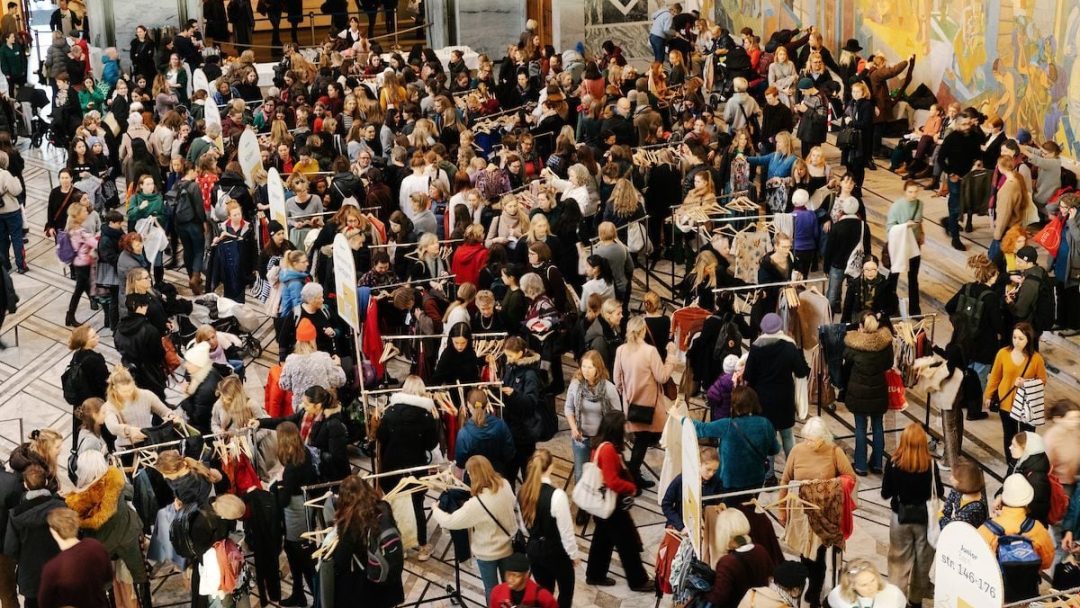 Under feiringen av miljøhovedstadsåret samles et stort publikum rundt klesstativer på et innendørs marked eller arrangement, opptatt med å surfe og samhandle i en hall utsmykket med forseggjort veggdesign.