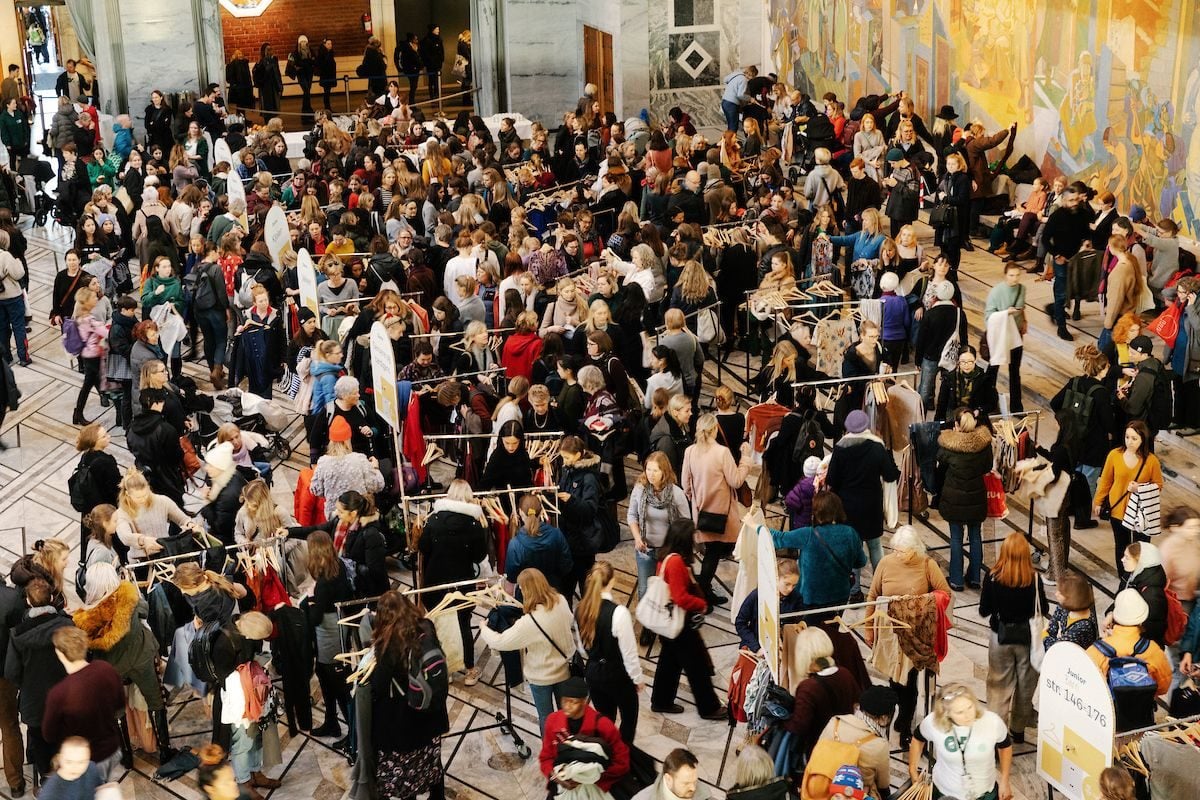 Under feiringen av miljøhovedstadsåret samles et stort publikum rundt klesstativer på et innendørs marked eller arrangement, opptatt med å surfe og samhandle i en hall utsmykket med forseggjort veggdesign.