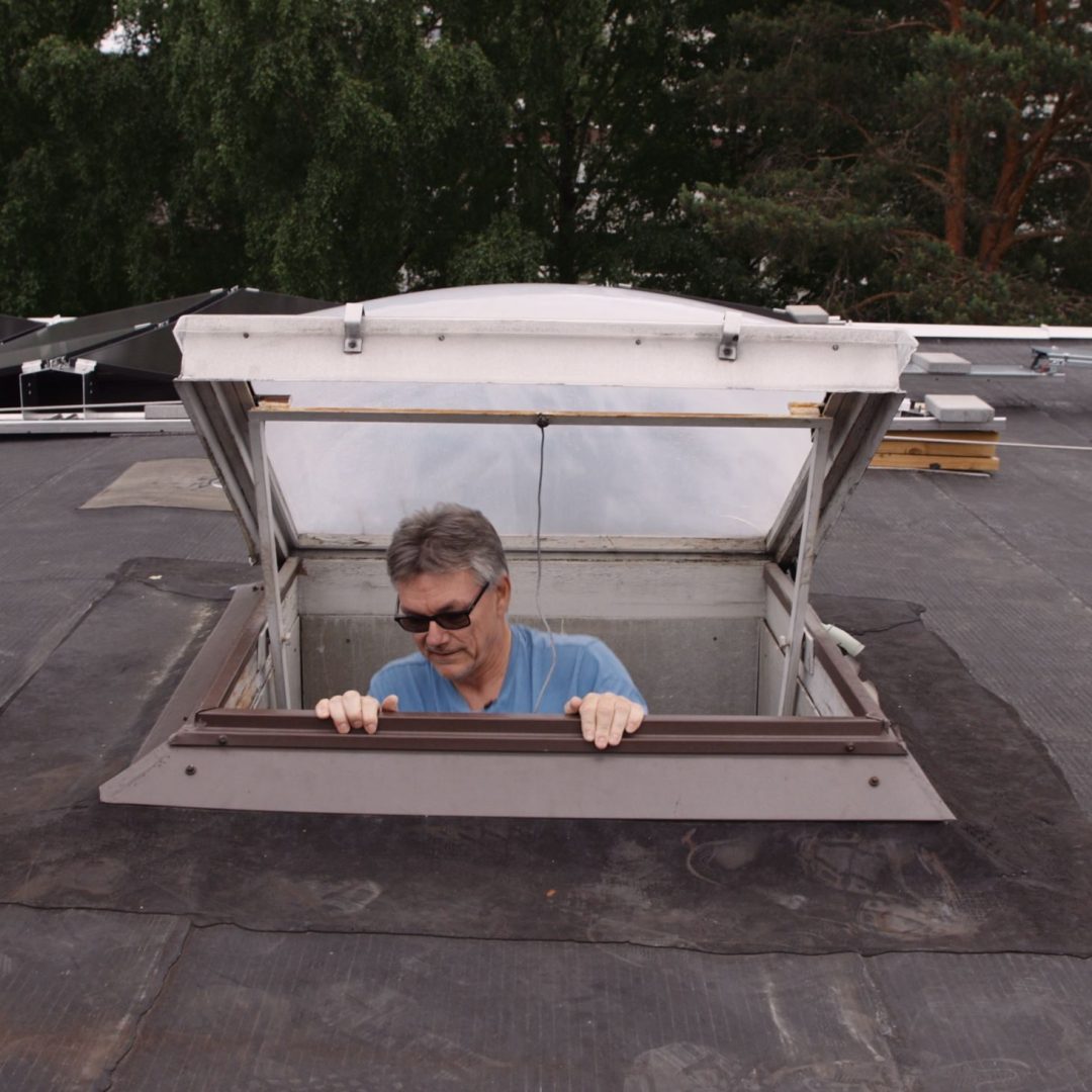 En mann titter ut av ei takluke på ei boligblokk