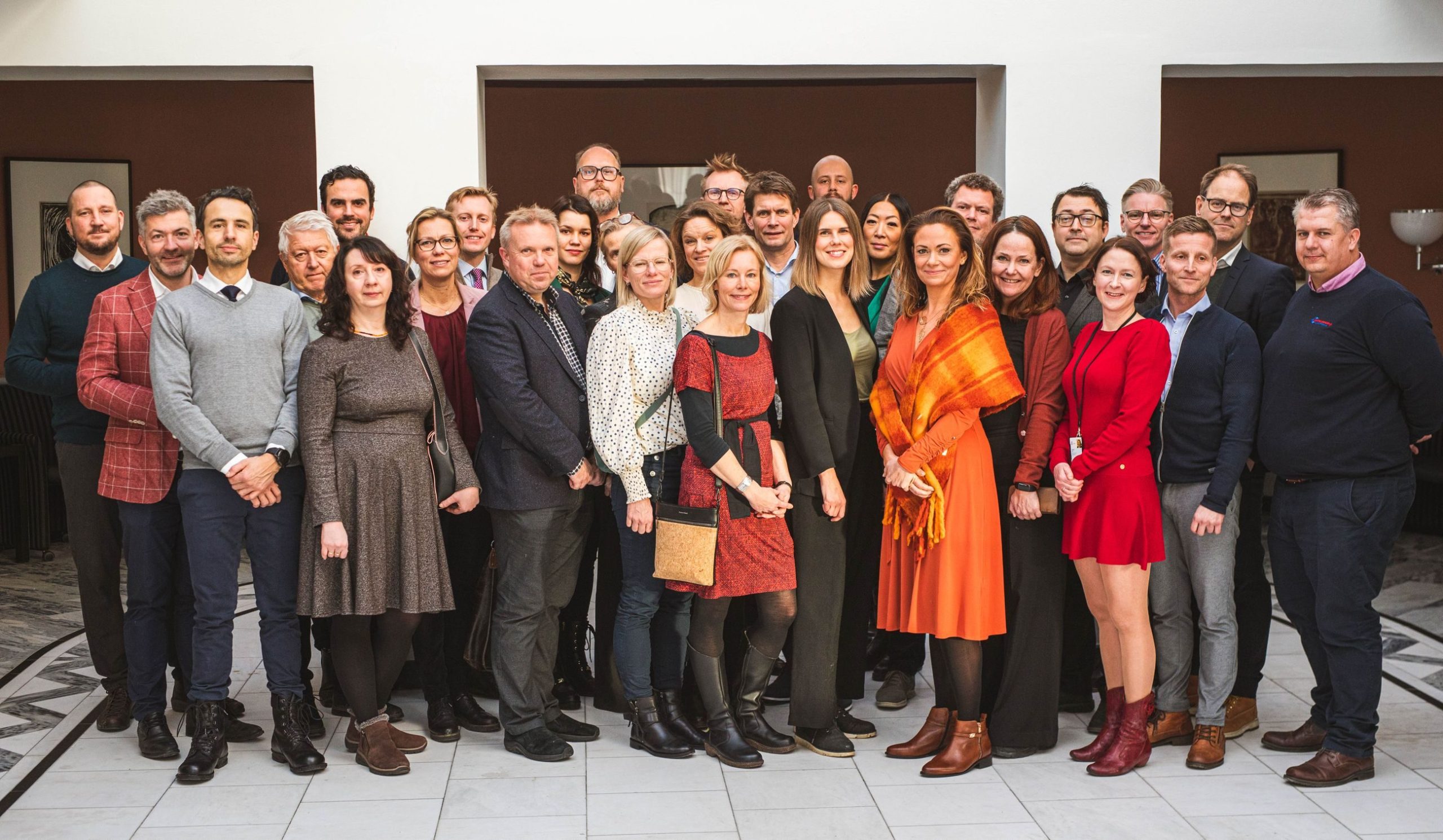 En mangfoldig gruppe mennesker som poserer sammen i et godt opplyst innendørsmiljø, med noen i formelle antrekk og andre i uformelle klær.