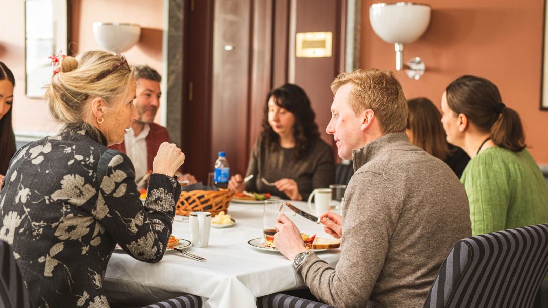 Gruppe mennesker sitter rundt et bord i en restaurant, engasjert i samtale og spising.