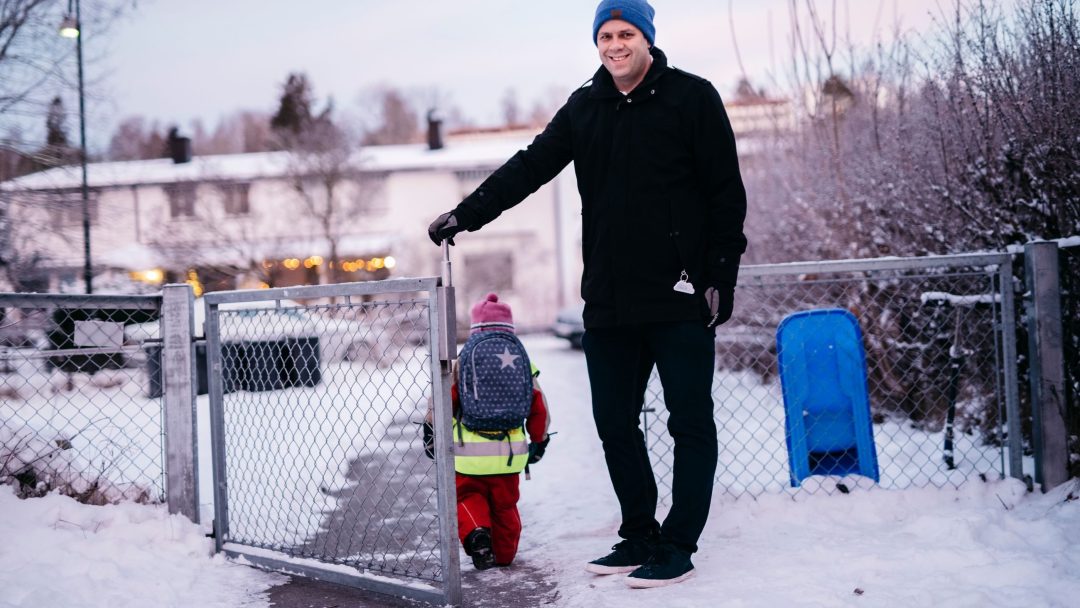 En voksen i mørke vinterklær og et barn i lyst vinterutstyr med en ryggsekk går gjennom en snødekt port, reisen deres minner oss subtilt om innsiktene fra klimasårbarhetsanalysen.