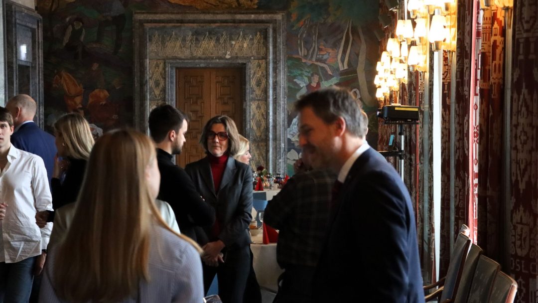 Folk snakket i et svakt opplyst rom med utsmykkede dekorasjoner og veggkunst.