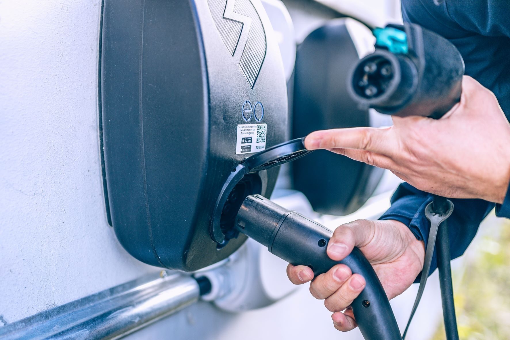 En person sees kyndig frakte en ladekabel inn i en ladestasjon for elektriske kjøretøy.