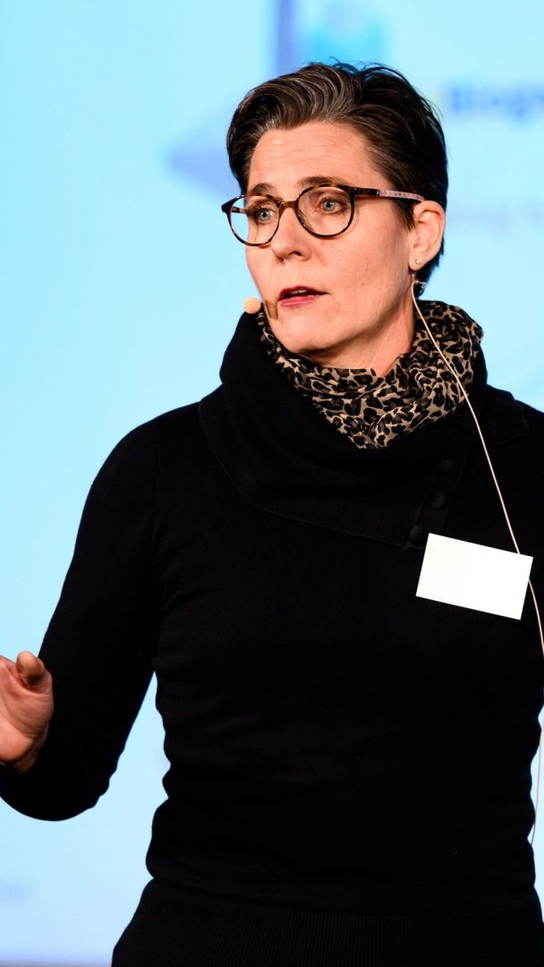 Person med briller og en svart topp som snakker med et mikrofonhodesett.