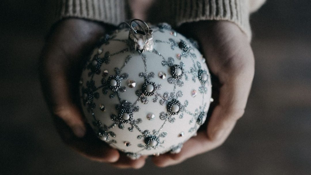 Hender som holder en utsmykket hvit julen ornament dekorert med intrikate perler og rhinestone mønstre.