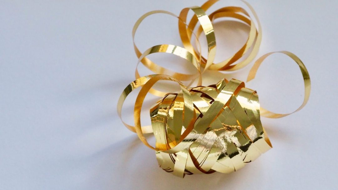 Et skinnende gyllent bånd, som minner om julens festligheter, krøllet og sammenfiltret på en hvit overflate.