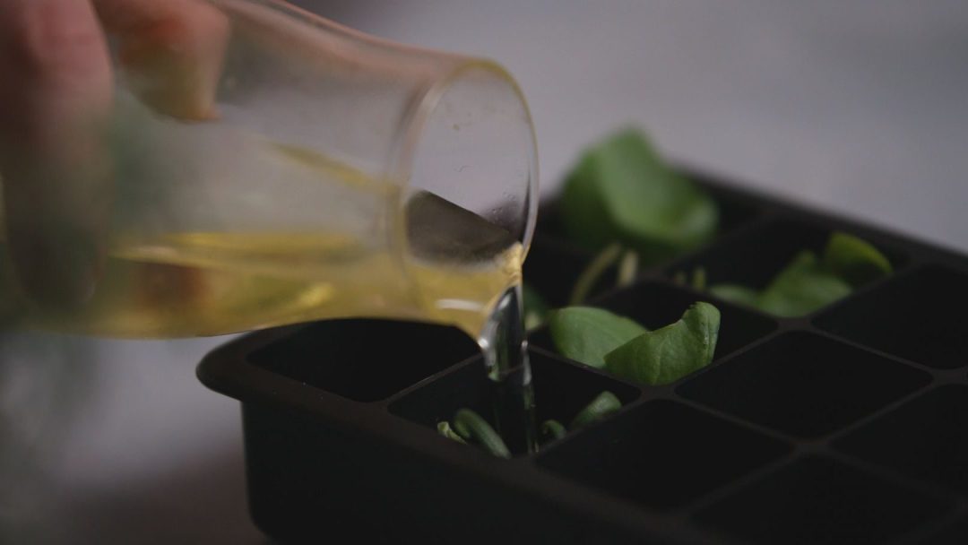 Å helle væske forsiktig i et elegant, svart isbitbrett fylt med levende grønne blader gir en festlig julen-touch.