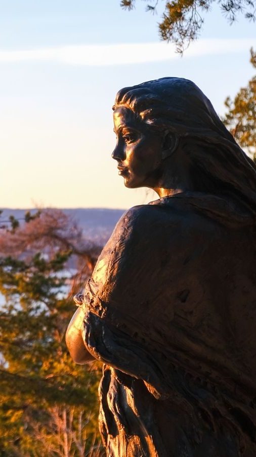 En bronsestatue av en kvinne med flytende hår, armene i kors, pryder scenen mot et bakteppe av vann og trær ved solnedgang. Dette fengslende synet er et av de beste Oslotipsene for alle som utforsker kunst sammenvevd med naturens skjønnhet.