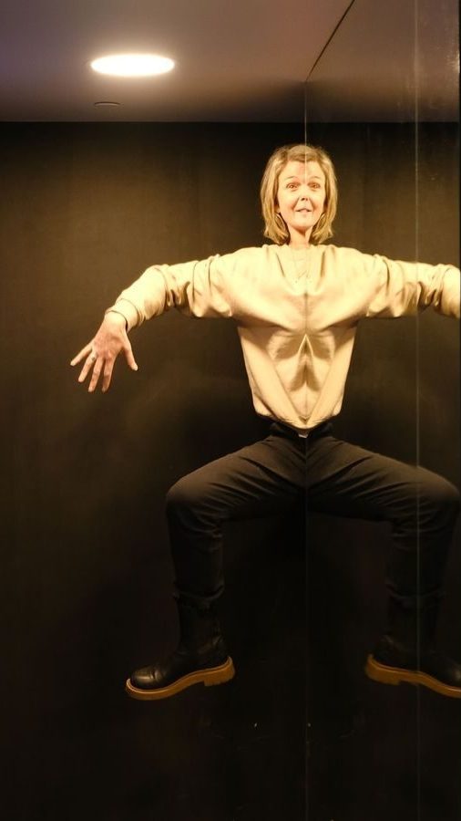 En person står med armer og ben spredt, silhuetten deres ligner en speilvendt edderkopp-lignende effekt mot en svart bakgrunn, en unnvikende Oslotips som fanger essensen av kunstnerisk symmetri.