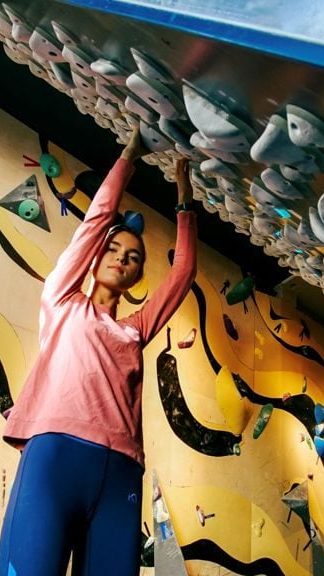 En person i en rosa langermet skjorte og blå bukser navigerer behendig i taket på en innendørs klatrevegg, og legemliggjør den eventyrlystne som inspirerte Oslotips.