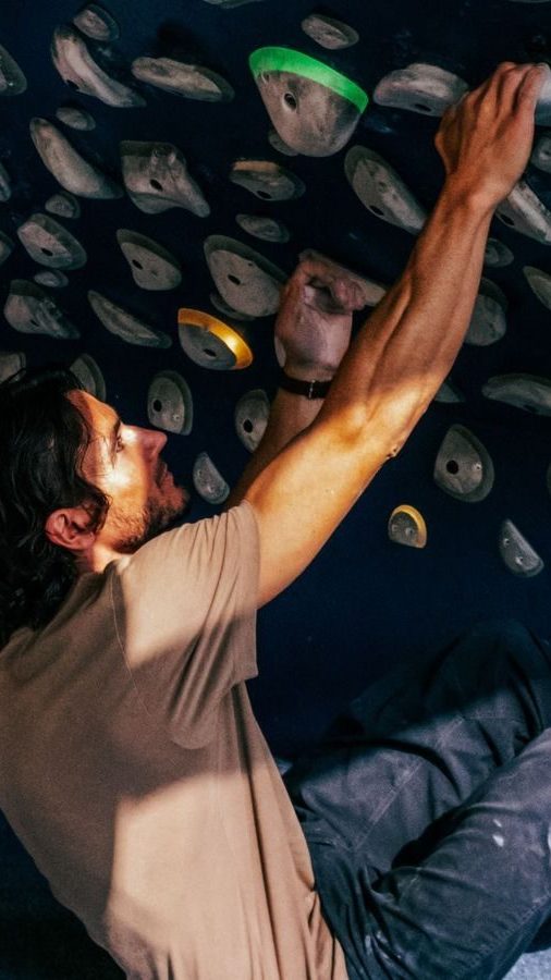 Person som klatrer på en innendørs buldrevegg ved Oslotips, griper fargerike håndtak med et fokusert uttrykk.