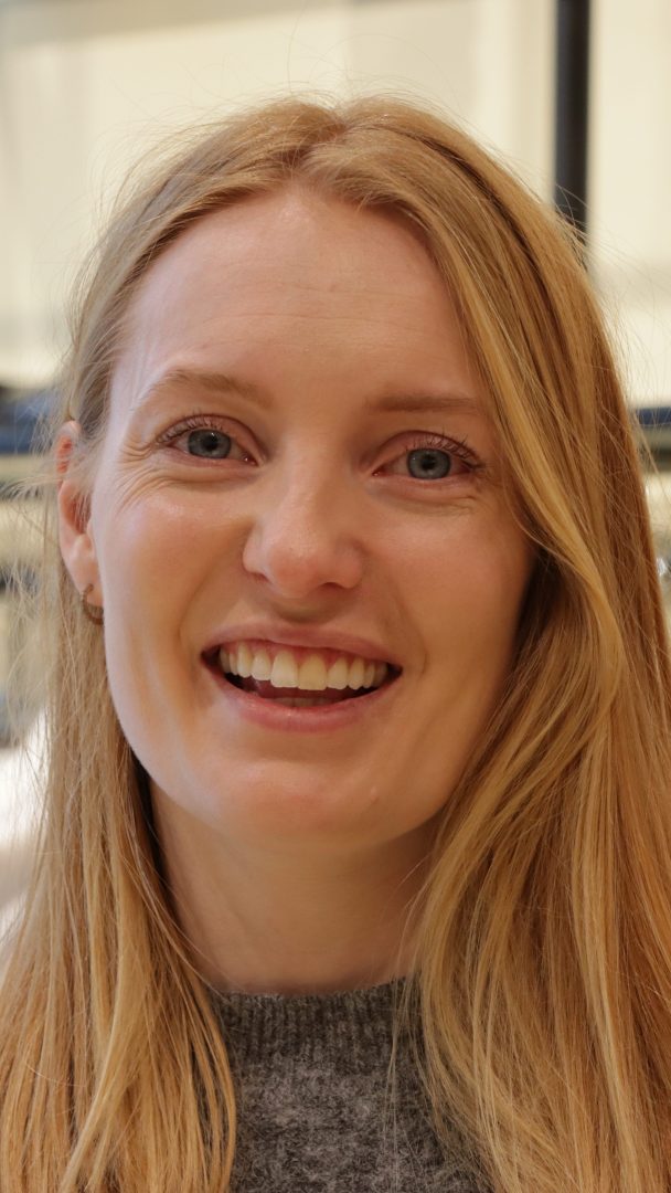 En person med langt blondt hår smiler til kameraet og stråler av glede som om hun nettopp har funnet en skjult skatt hos en bruktbutikk.