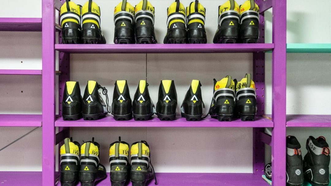 Rader med sorte og gule skistøvler, tilgjengelig for låne sportsutstyr, er pent arrangert i lilla hyller.