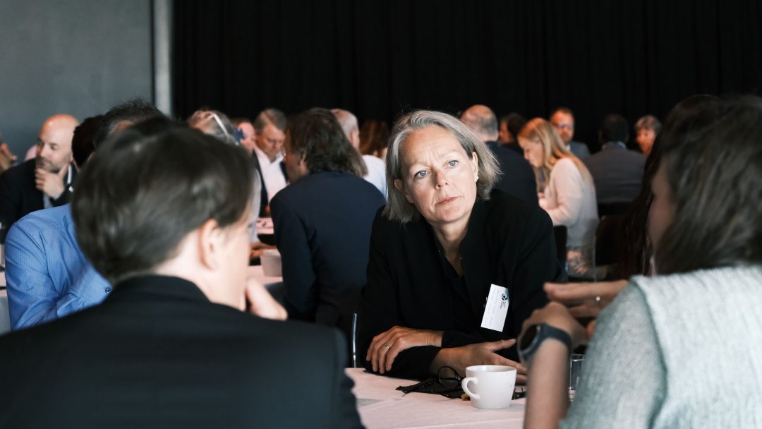 Folk satt rundt et bord, engasjert i samtale på en konferanse.