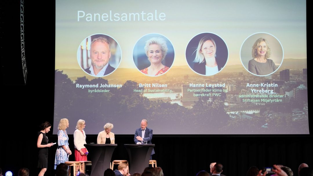 Panelsamtale med fem personer på scenen. Stor skjerm i bakgrunnen viser navn og titler på fire paneldeltakere.