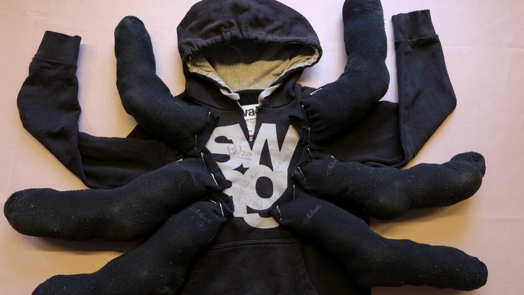 Denne grå hettegenseren, perfekt for en halloweenkostyme, har et SWO-trykk med seks svarte sokkerfylte armer festet, som etterligner utseendet til en edderkopp.