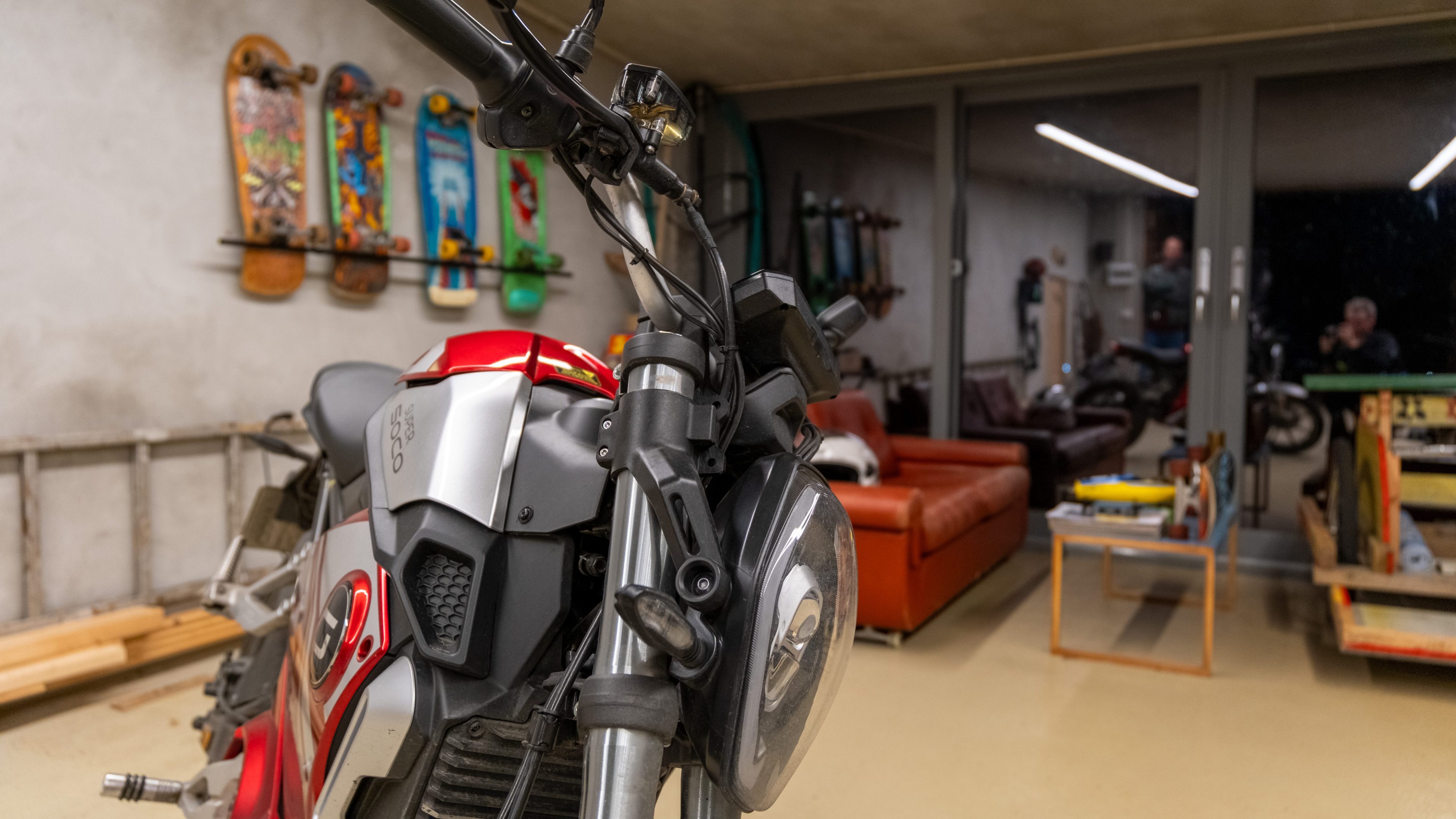 En elmoped hviler i garasjen, flankert av skateboarddekk på veggen og en koselig sittegruppe med sofa.