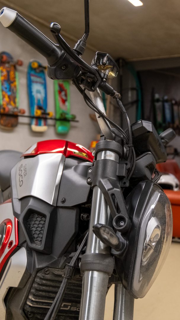 Nærbilde av en rød og sølvfarget motorsykkelfront i en garasje med ulike skateboards og en elmoped montert på veggen i bakgrunnen.