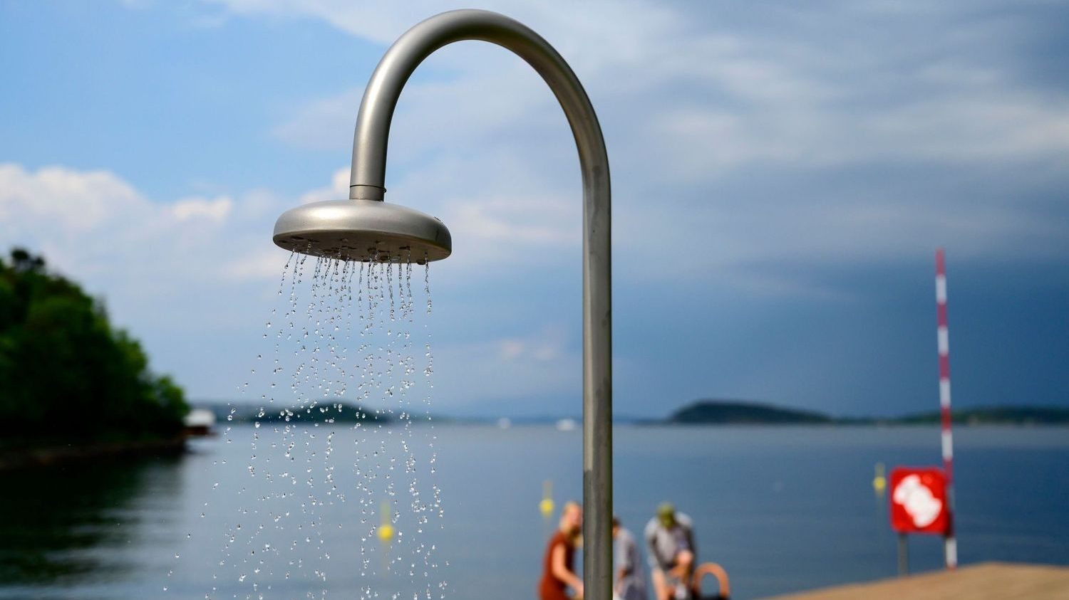 En dusj det kommer vann ut av. Folk og havet i bakgrunnen.