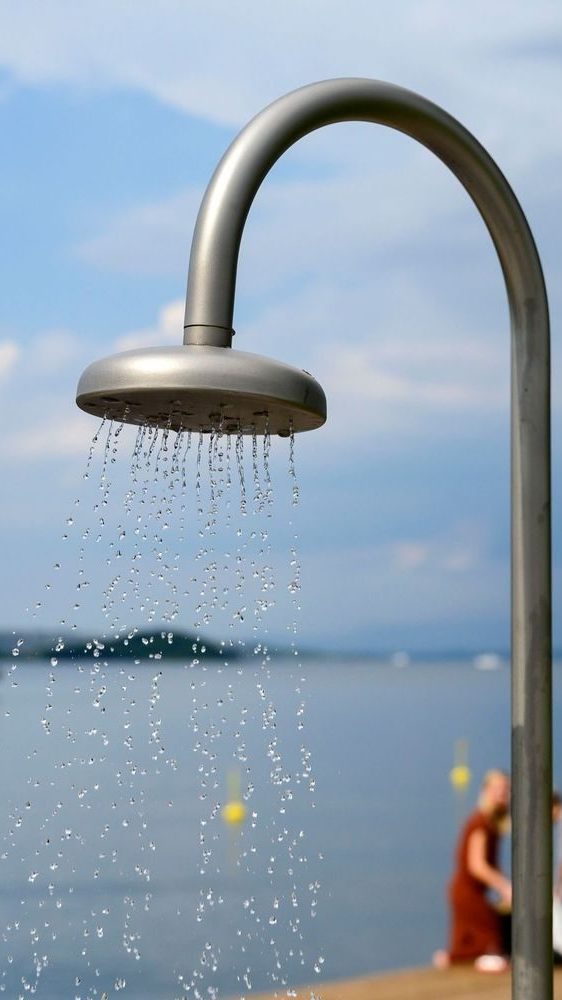 Et utendørs dusjhode fosser ned vanndråper, satt mot en uskarp innsjø – et perfekt tillegg til populære badeplasser, der overskyet himmel forsterker den rolige stemningen.