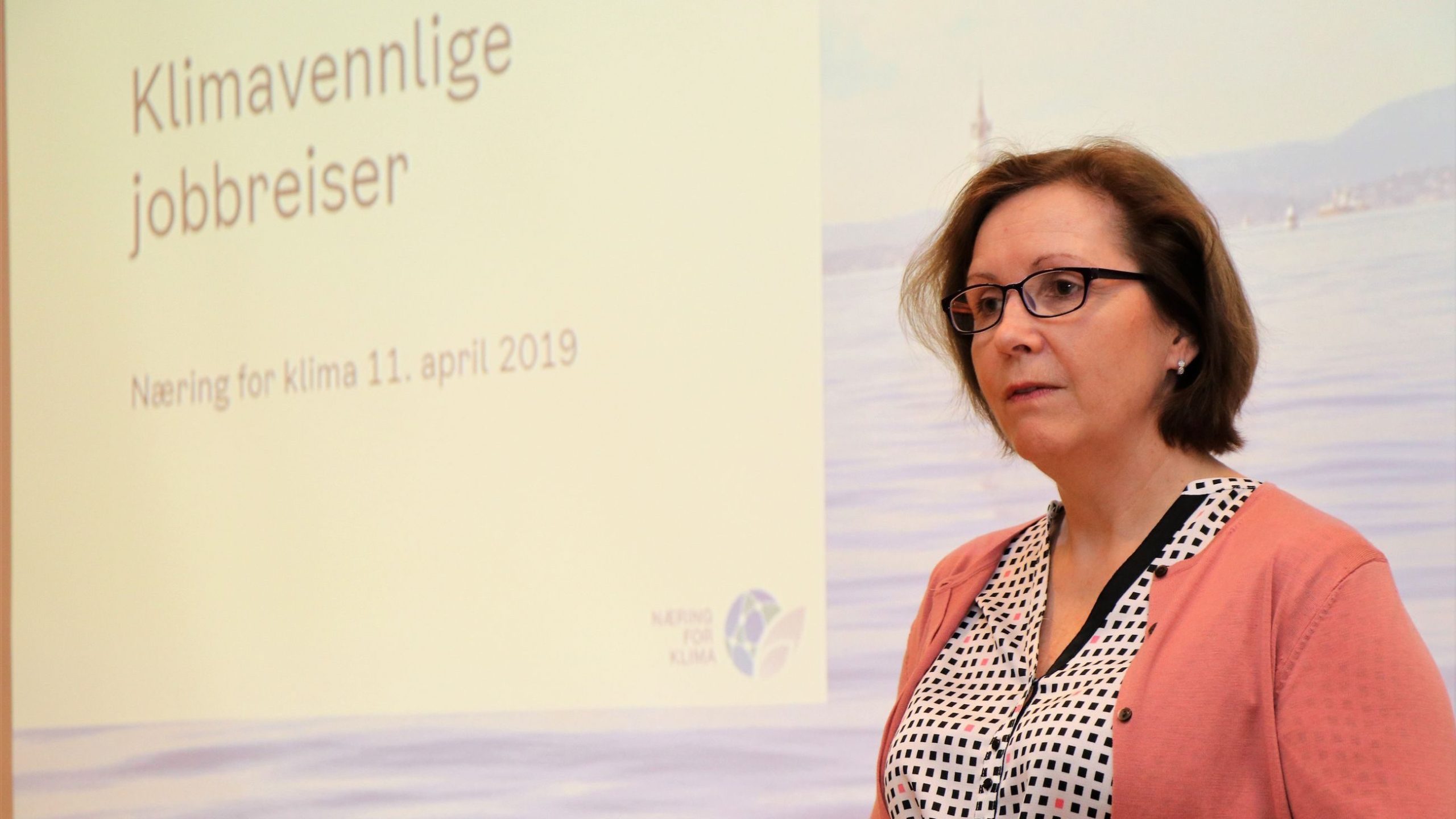 En kvinne står foran en presentasjonsskjerm som viser «Klimavennlige jobbreiser» og «Næring for klima 11. april 2019.