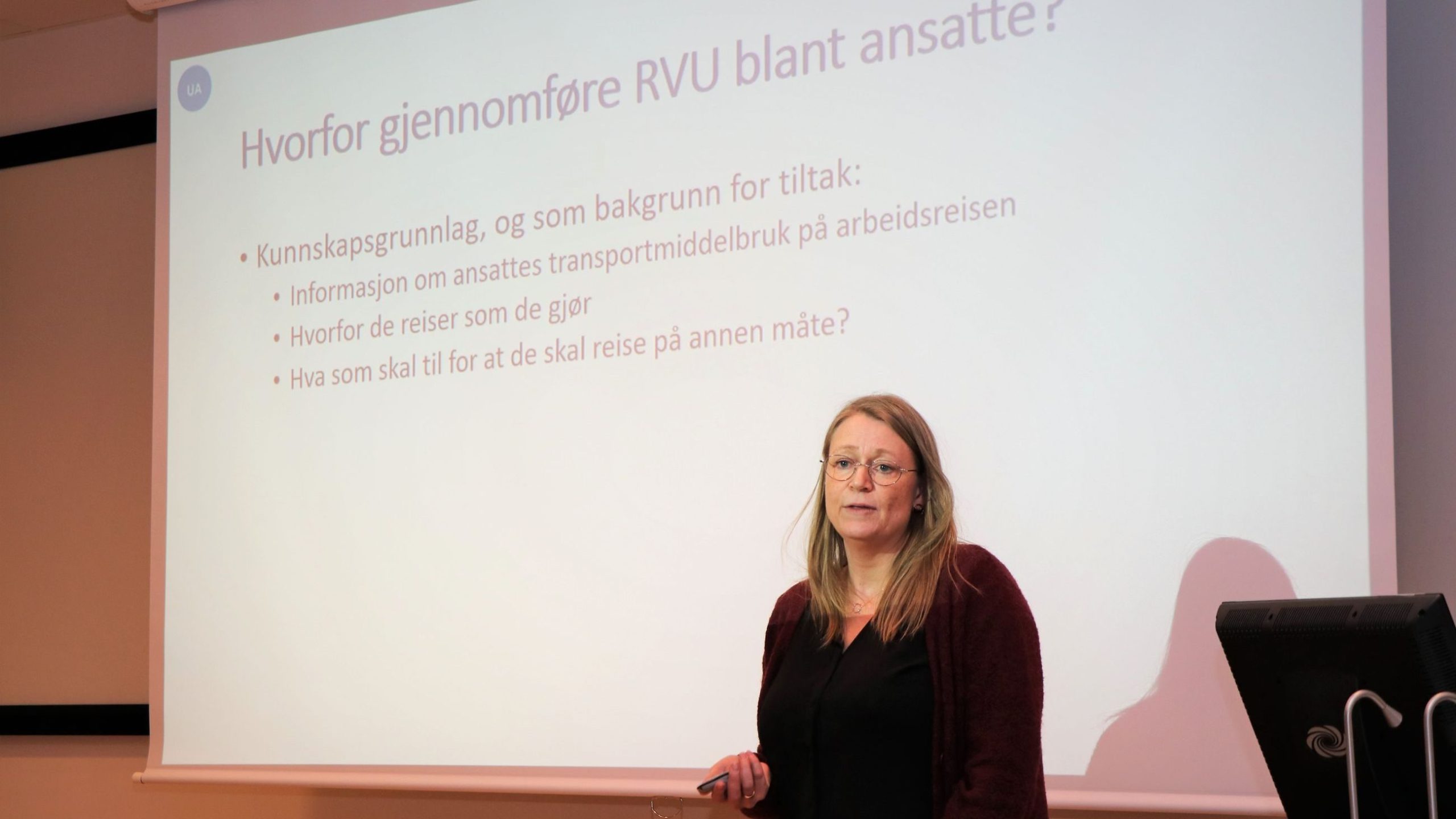 En kvinne presenterer foran en skjerm som viser et lysbilde på norsk.