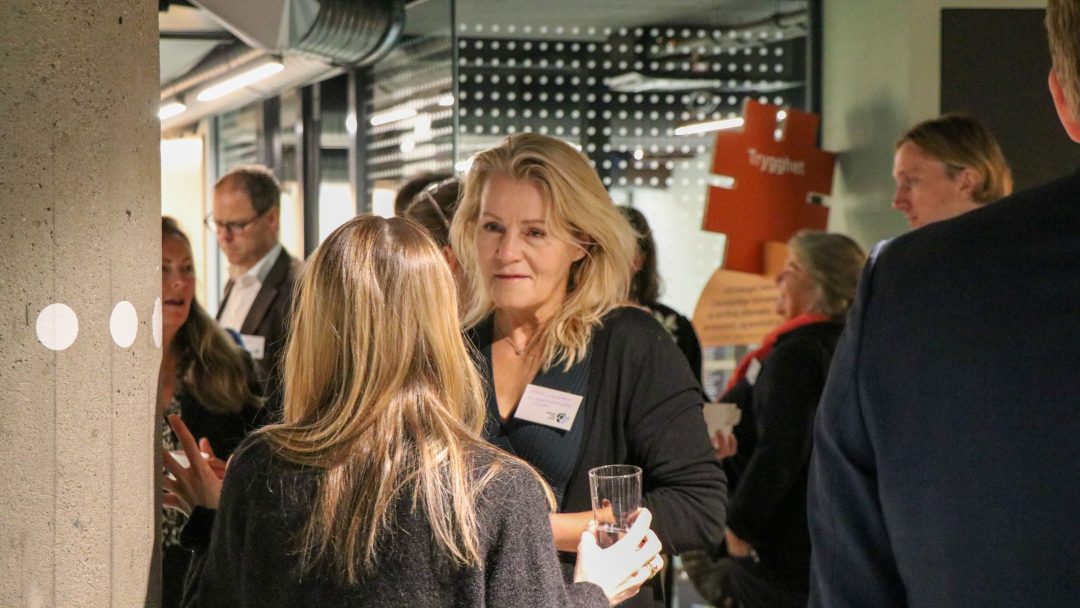 Folk sosialiserer seg på et innendørsarrangement, med flere personer som deltar i samtale og holder drinker.