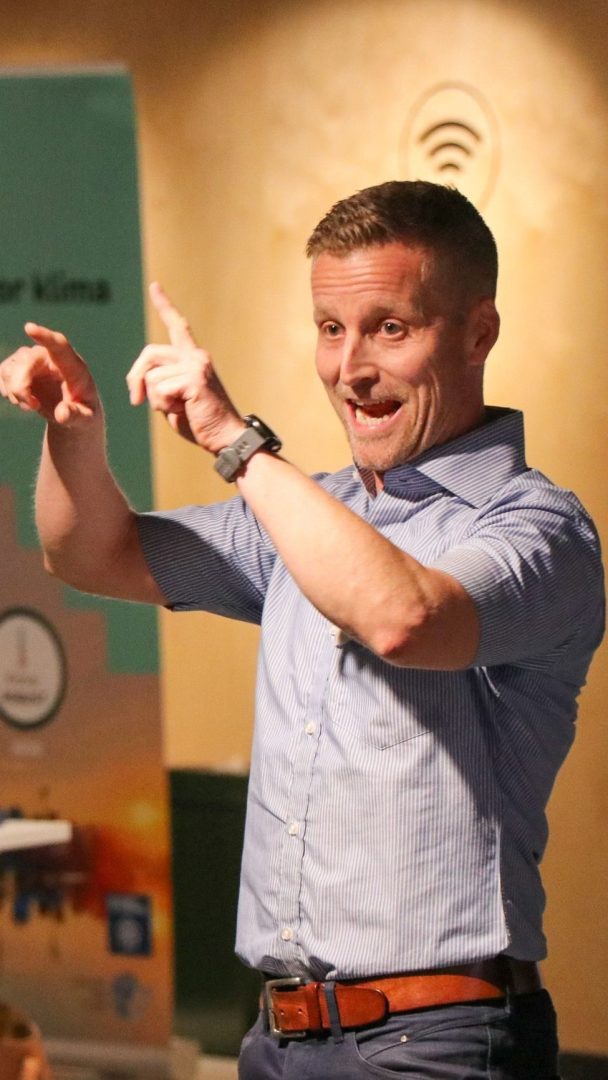 Person i blåstripet skjorte gester animert mens han snakker innendørs.