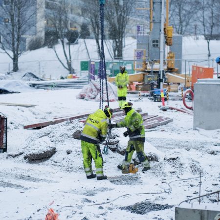 Bygningsarbeidere som jobber på en utslippsfri byggeplass i snøen. Construction workers on a building site covered in snow.