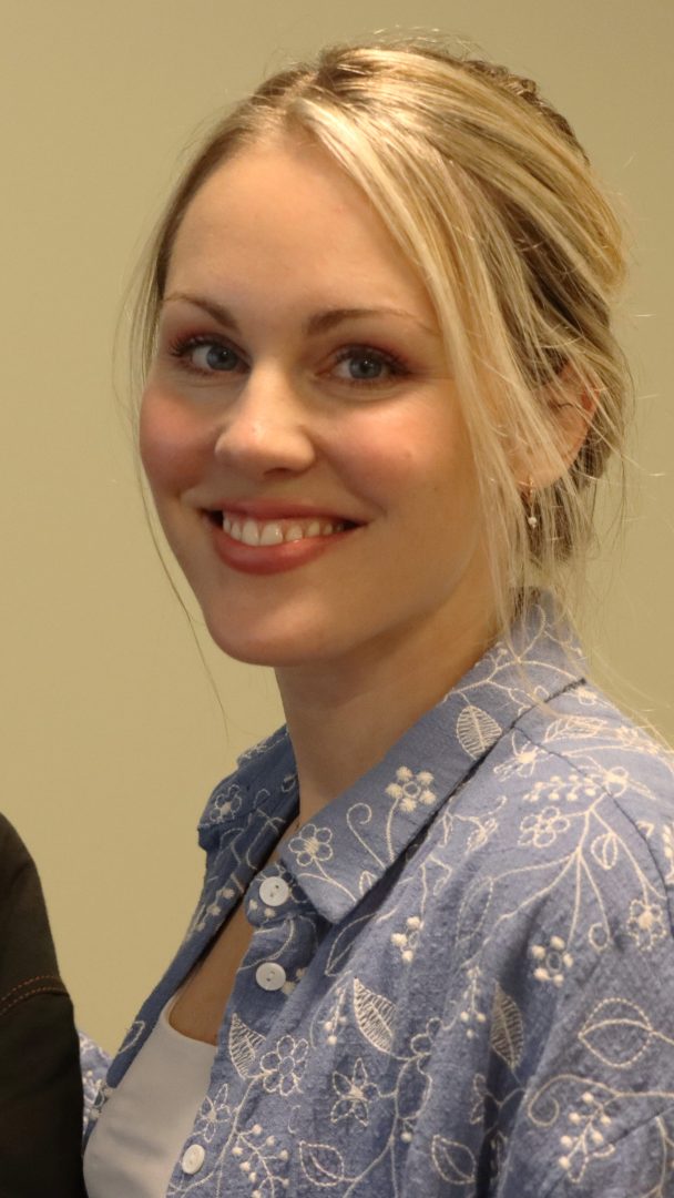 Kvinne med blondt hår smilende, ikledd en blå blomstermønstret skjorte hun fant i en lokal bruktbutikk.