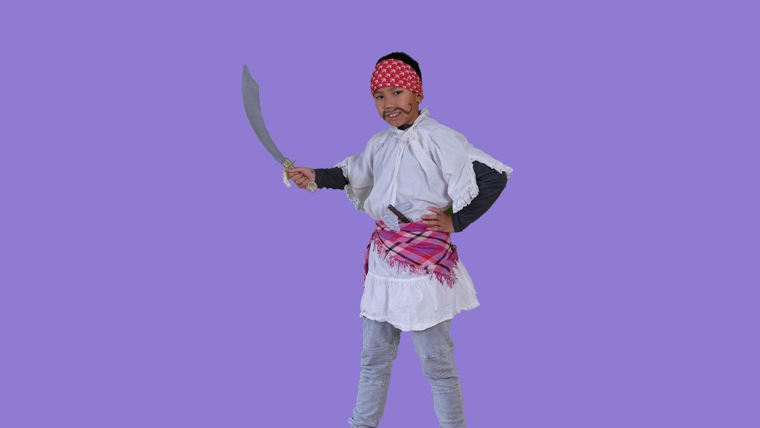 Et barn i en halloweenkostyme piratkostyme stiller seg med et buet sverd mot en solid lilla bakgrunn.