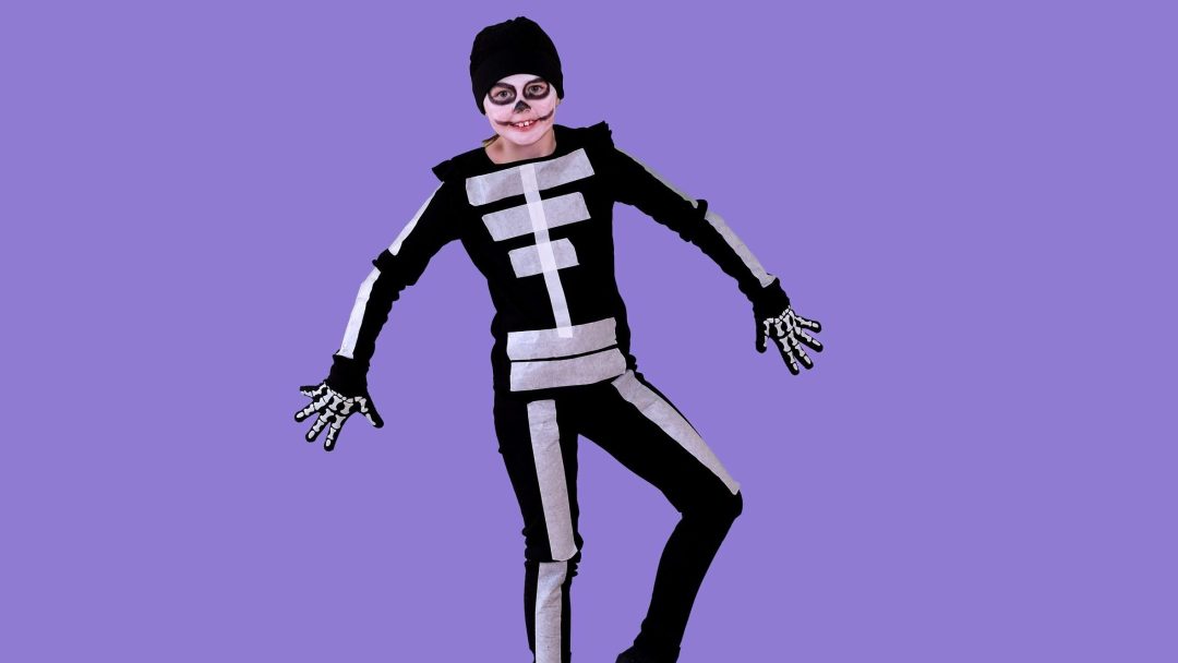 Et barn i et svart skjelettkostyme med sølvaksenter og ansiktsmaling poserer med armer og ben spredt, og legemliggjør ånden til en Halloweenkostyme mot en livlig lilla bakgrunn.