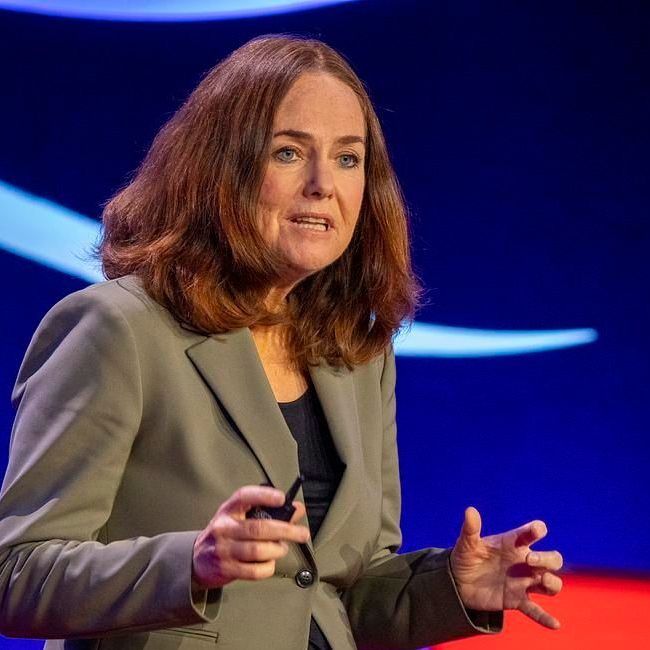 En kvinne med skulderlangt brunt hår snakker på scenen, iført en grå blazer, og diskuterer lidenskapelig den raske transformasjonen av byer.