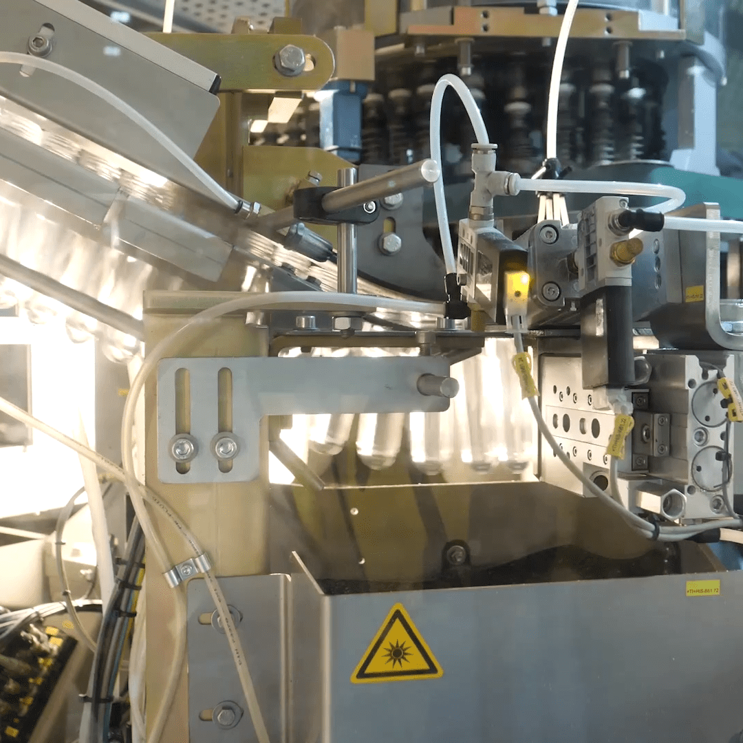 Midt i industrimaskineriet som er i drift, flettes metallkomponenter og rør sammen, med sikkerhetsadvarselsskilt fremtredende. Noen deler er laget av resirkulert plast, som viser en forpliktelse til bærekraft i dette robuste miljøet.