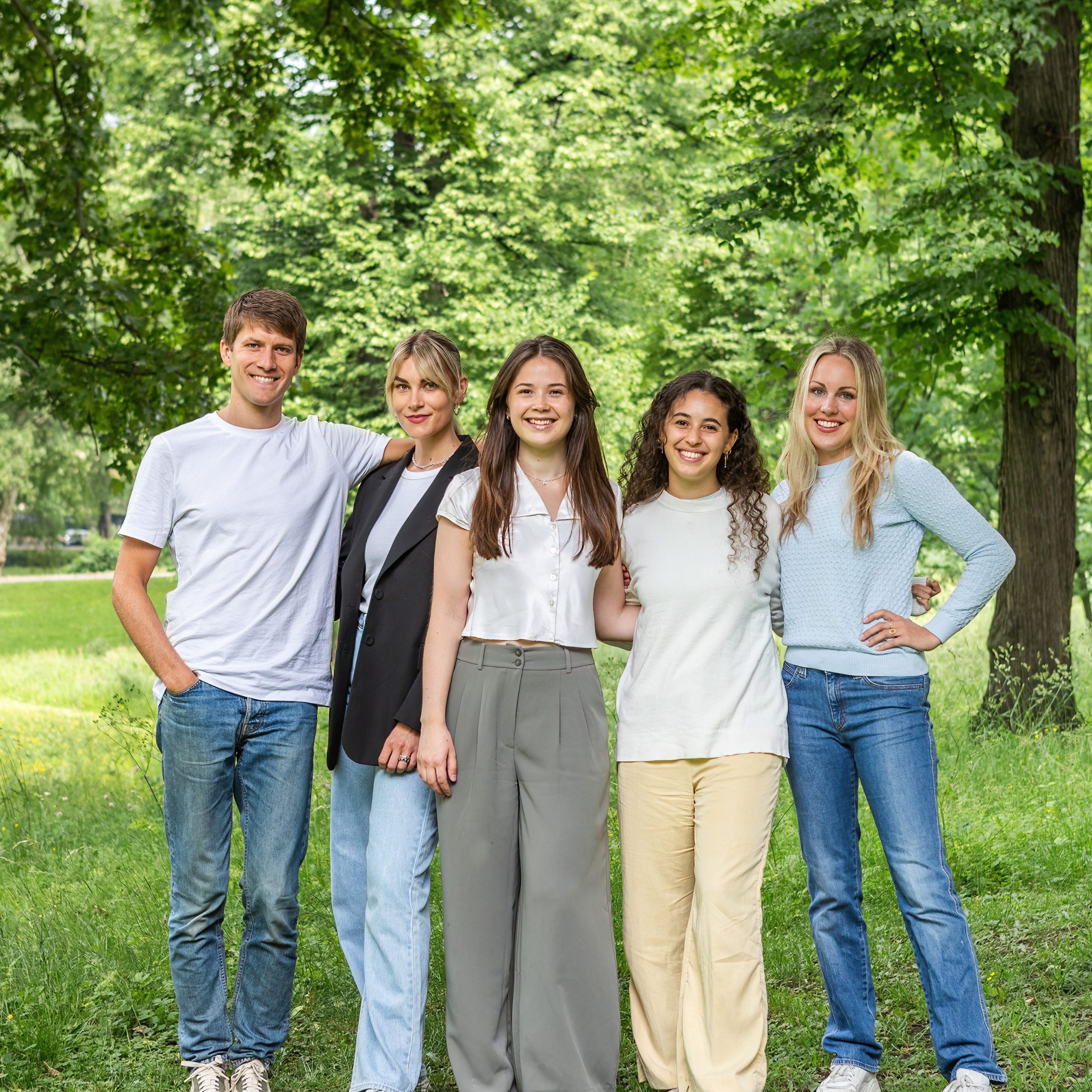 Fem Klimapilotene-deltakere står sammen utendørs på gress, omgitt av trær, og smiler varmt til kamera.