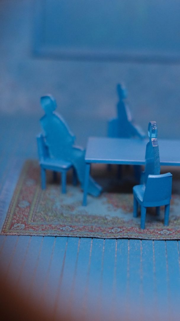 Tre blå figurer sitter rundt et bord på et teksturert teppe i det blåtonede rommet til Klimahuset, og skaper en atmosfære som gjenspeiler naturens rolige harmoni.