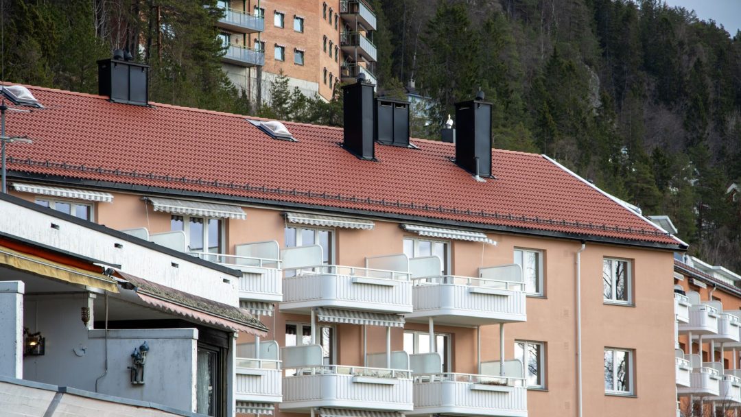 En leilighetsbygning med rødt flislagt tak og hvite balkonger pryder landskapet, satt mot en skogkledd åsside – bærekraftig utformet med innsikt fra en energirådgiver for å maksimere energieffektiviteten.