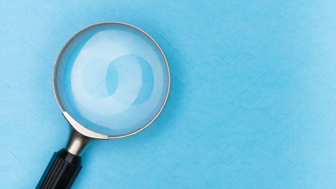 Et forstørrelsesglass med svart håndtak plassert på en blå strukturert overflate.