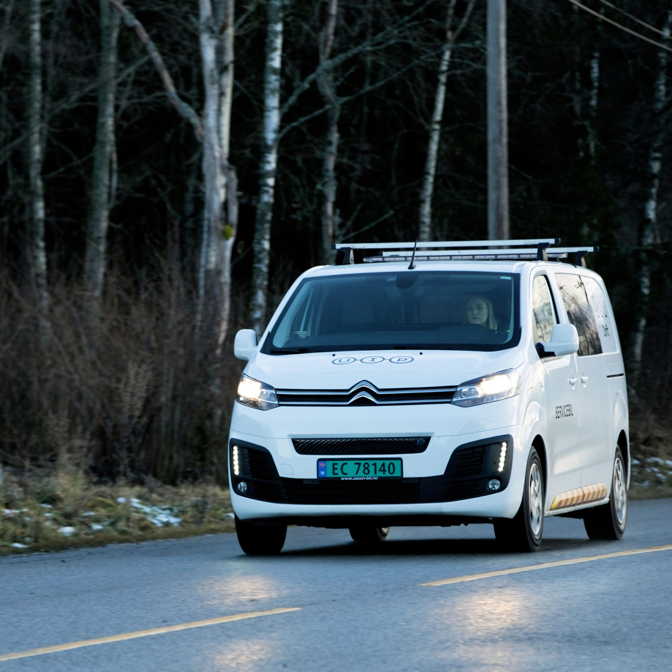 En hvit Citroën-varebil glir langs en asfaltert vei, innrammet av frodige trær i bakgrunnen, potensielt en del av de effektive transportløsningene som er understreket i Oslopakke 3.